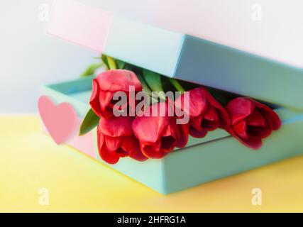 gift box with bouquet of tulips and red heart on yellow background closeup Stock Photo