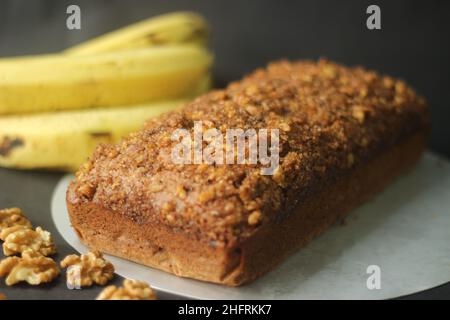 Banana bread made with wholewheat flour and coconut oil. Baked with cinnamon, sugar and walnut for a crunchy top. Shot with bananas on black backgroun Stock Photo