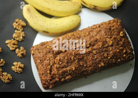 Banana bread made with wholewheat flour and coconut oil. Baked with cinnamon, sugar and walnut for a crunchy top. Shot with bananas on black backgroun Stock Photo