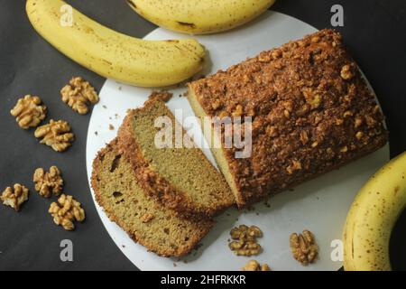 Banana bread made with wholewheat flour and coconut oil. Baked with cinnamon, sugar and walnut for a crunchy top. Sliced banana bread shot with banana Stock Photo