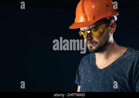 Male electrician in a protective helmet with glasses on a black background. Stock Photo