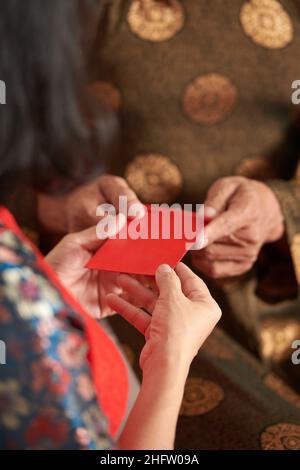Hands of senior man giving red envelope to his adult daughter for Chinese New Year Stock Photo