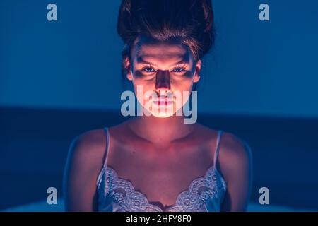 Horror. The woman shines a flashlight at herself from below and creates a scary face. Scary girl with dark hair. Scare. Stock Photo