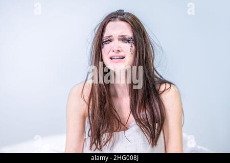 Get the bad news. A woman with a face dirty from mascara sits in bed, crying. Depression. Get upset. Heartbroken. To suffer. Broken heart. Stock Photo