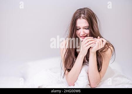 A woman with a face dirty from mascara sits in bed, crying. Heartbroken. Depression. Get the bad news. To suffer. Broken heart. Get upset. Stock Photo