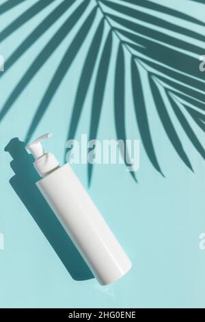 Bottle of cream with palm leaf shadow on blue background Stock Photo