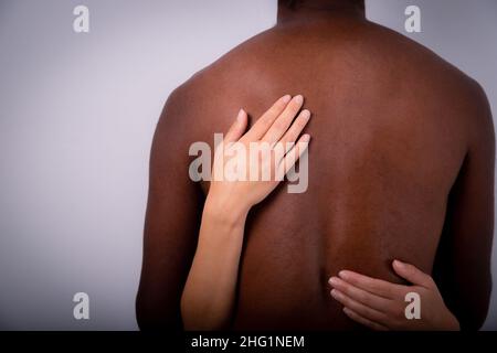 Close-up of a Caucasian woman's hands touching an African man's back. Interracial. Couple of different ethnicity hug each other. Focus on the woman's Stock Photo