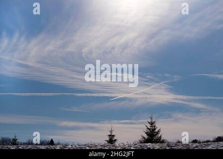 Cirrus and cirrostratus clouds crossed by jet airplane contrails over the top of a ridge. Stock Photo