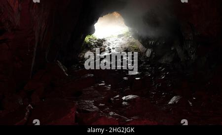 View from inside a cave with rocky path and daylight at the entrance. Unknown underground tunnel, dangerous travel concept. Stock Photo
