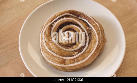 Top view of tasty bun snail with white glaze rotating while lying on a glass plate. Close up of the sweet pastry product, foodporn concept Stock Photo