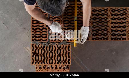 Close up of an industrial worker making wall with mortar and bricks, using hammer and level tool. Male hands building exterior walls, using hammer for Stock Photo