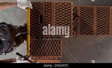 Top view of an industrial worker making wall with mortar and bricks, using hammer and level tool. Male hands building exterior walls, using hammer for Stock Photo