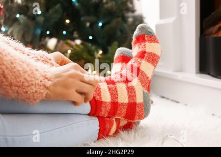 Woman in warm socks near fireplace at home on Christmas eve, closeup Stock Photo