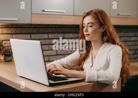 Redheaded businesswoman working on computer sitting at desk in the morning. Girl studying online. Online education, remote work. Stock Photo