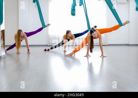 Three yogi women makes side splits using blue hammock for aerial fly yoga. Concept wellness yoga, group training. Stock Photo
