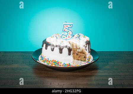 A birthday cake, missing a slice, bears a candle in the shape of the number 5. Stock Photo