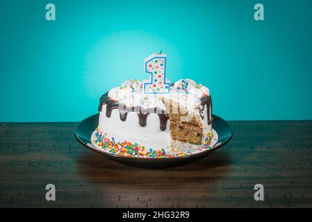 A birthday cake, missing a slice, bears a candle in the shape of the number 1. Stock Photo