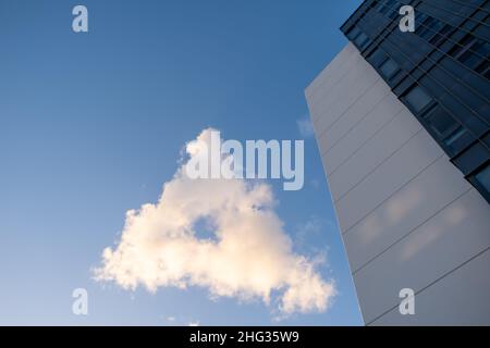Triangle shaped cloud against blue sky at sunset with modern residential building - looking up Stock Photo