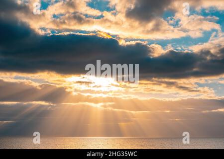Setting sun rays beaming through beautiful clouds over water Stock Photo