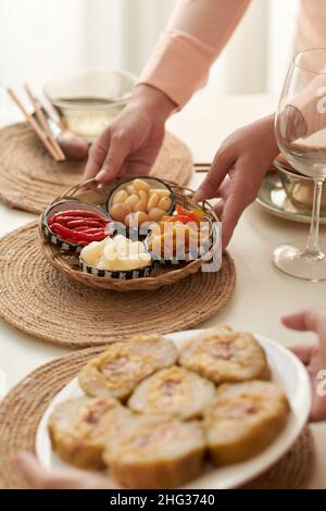 Hands of woman putting plate with pickled vegetables on table served for Chinese New Year dinner Stock Photo