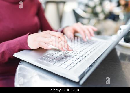 Crop unrecognizable female browsing modern netbook while sitting at table on terrace of outdoor cafe in city on blurred background Stock Photo