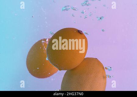 Lemons fall into the water. On the background of gradient pink and blue light Stock Photo