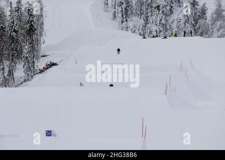 Vuokatti, Finland - January2022: Young boy in mid-air jump in a slopestyle terrain park while his friends watch on the top of the slope in Vuokatti sk Stock Photo
