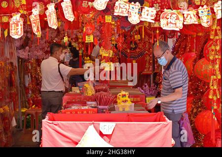 People with masks shopping for Chinese New Year ornaments in a bright scarlet colored stall in Singapore's Chinatown to usher the Tiger Year 2022 Stock Photo