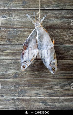 Dried salty river fish hanging on a twine on a wooden background. Vertical view Stock Photo