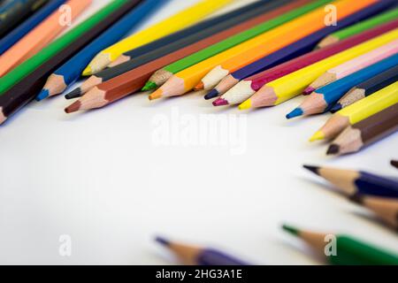 Colored pencils on a white table are scattered in a semicircle with space for text. Stock Photo