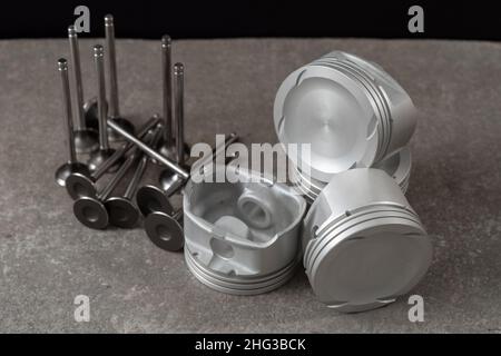 Set of new car pistons and valves on concrete gray background, car repair parts. Stock Photo