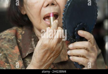Elderly woman applied lipstick and looked in the mirror. Stock Photo