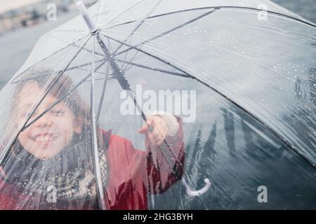 front view closeup portrait of happy little girl dressed in red and holding a transparent umbrella with rain drops Stock Photo