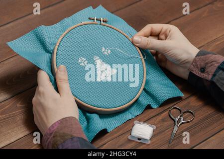 Woman holding wooden hoop with cross-stitch pattern and needle in her hands. Stock Photo