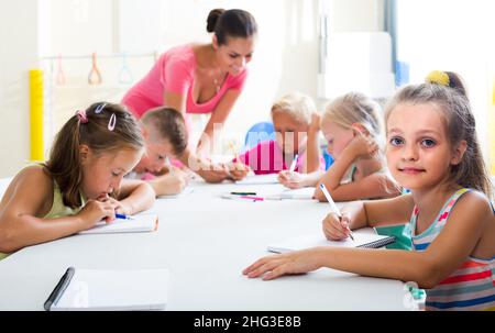 children making writing exercises with help of teacher in class Stock Photo