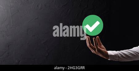 Hand holds green icon Check mark,Check Mark Sign, Tick Icon,right sign,circle green checkmark button,Done.On dark background.Banner.Copy space.Place f Stock Photo