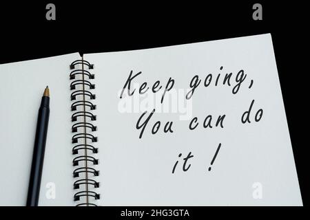 Top view of white notebook with motivational quote on dark background - Keep going you can do it. Stock Photo