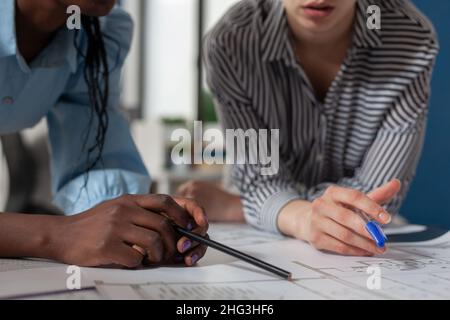 Closeup view of mixed race architects holding pencil and pen over blueprints at architectural desk. Detail of engineer hands over technical drawing construction plans of residential project. Stock Photo