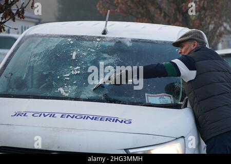 Windsor resident William McCarthy clears frost from the windscreen of his van in Windsor, Berkshire, as the country wakes up after a night when temperatures again dipped below freezing. Picture date: Tuesday January 18, 2022. Stock Photo