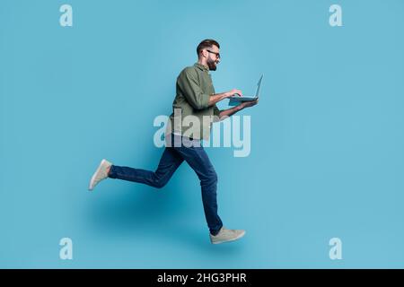 Profile photo of nice freelancer guy jump hold netbook typing email wear specs green shirt isolated blue color background Stock Photo