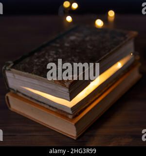 Two books stacked on a table and inside one of them there is a light Stock Photo