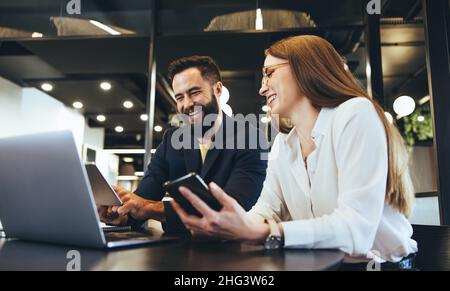 Smiling entrepreneurs using wireless technology while working together in an office. Two happy businesspeople looking at a digital tablet while sittin Stock Photo