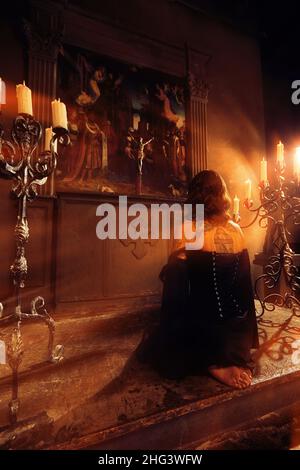 Prayer in church. Barefoot woman with dark hair kneeling in the Church, lights a candle and prays in front of the icon. Stock Photo