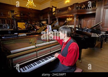 Piano tuner is tuning a grand piano by hand ay the Yamaha shop in London . Stock Photo