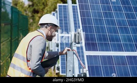 businessman in hardhat checking wires and holding folder near solar batteries outside Stock Photo