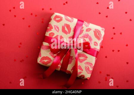 Valentines Day gift box with red ribbon on red background decorated heart shaped confetti. Flat lay, top view. Love and romance concept. Stock Photo