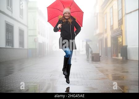 happy adult woman with jumped red umbrella on a rainy and foggy day Stock Photo