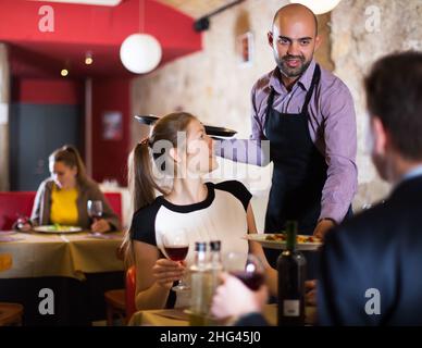 waiter bringing ordered dishes to smiling couple Stock Photo