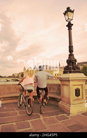 Couple on bikes watching sunset over Paris and Seine river from Pont Neuf, romantic scene in the french city of love Stock Photo