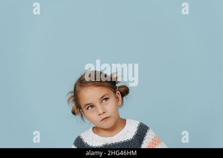 Looking up tight-lipped little girl in striped sweater, hair in buns over blue. A lot of copy space around. Stock Photo